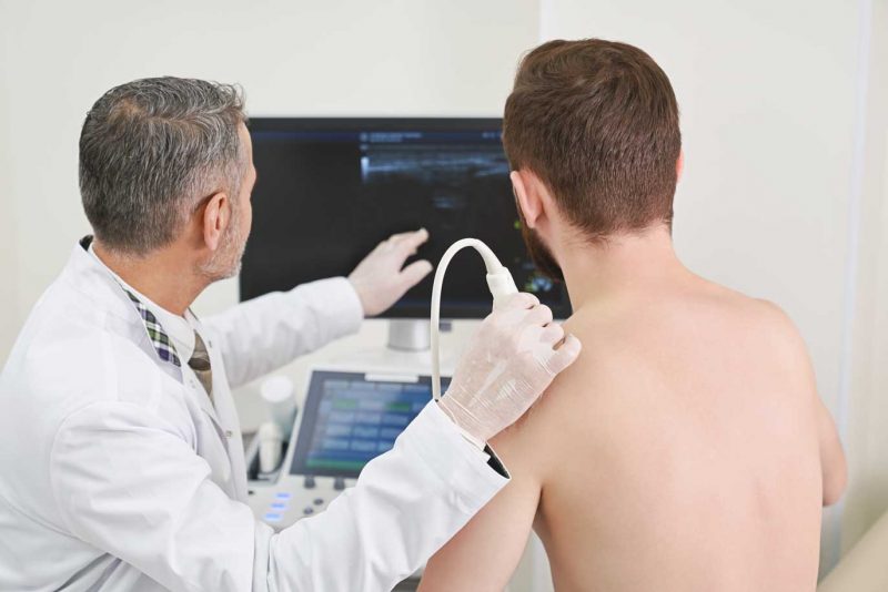 A radiológus mutatja a páciensnek az ízületi elváltozást az ultrahang monitoron